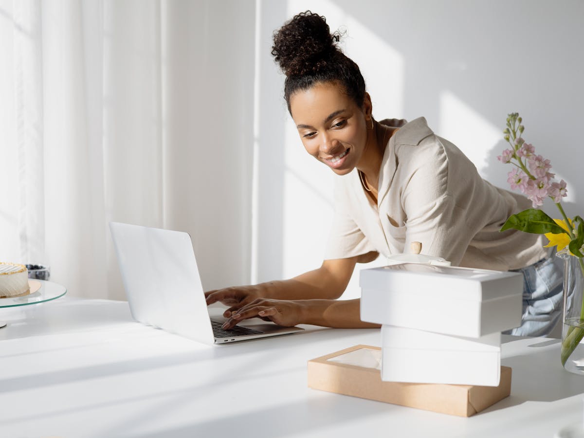A smiling small-business owner managing online orders on her laptop beside packed parcels
